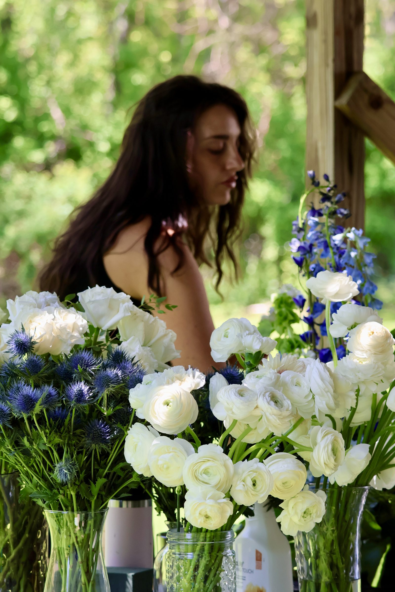 The florist working behind vases of white ranunculus, roses and blue thistle